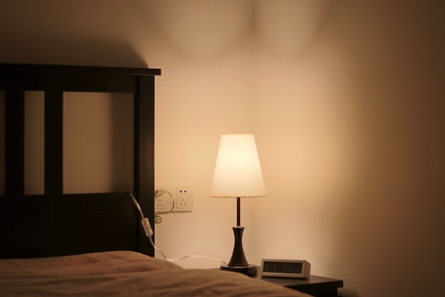 A cozy bed with a lamp on it, illuminating a dark room.jpg